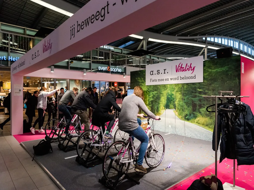 asr_vitality_fietsactivatie_popup_1024x768 Bezoekers nemen deel aan een interactieve fietsactivatie van a.s.r. Vitality in een winkelcentrum, waarbij zij op hometrainers fietsen als onderdeel van een merkactivatie.