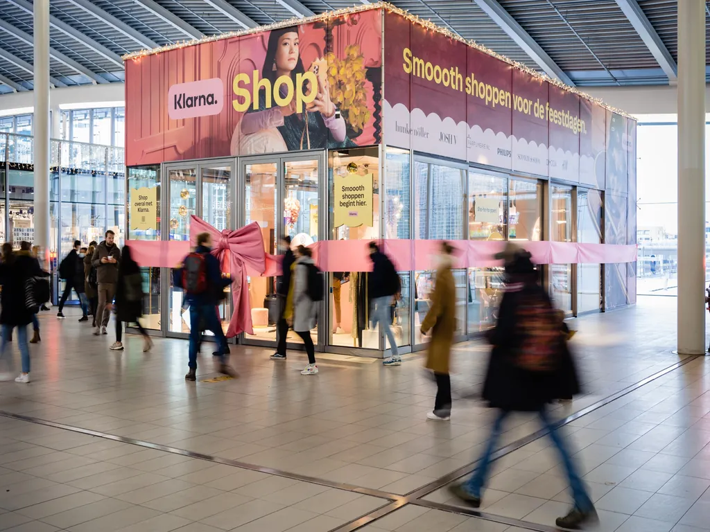 Klarna pop-up store in een winkelcentrum met feestelijke branding, waar bezoekers gebruikmaken van een tijdelijke winkelervaring tijdens de feestdagen.